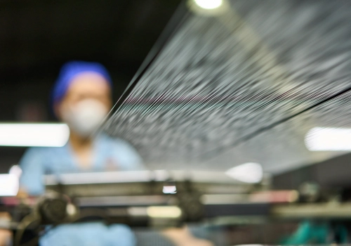 A worker blurred with a close up shot of strings of polyester yarn