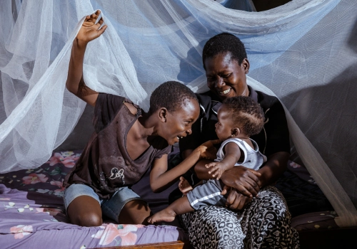 Two children and their mother under a mosquito net