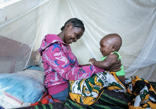 A mother smiling holding her happy baby on a bed under a mosquito net.
