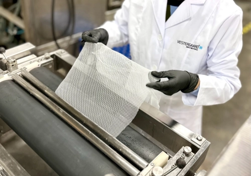 A person in a Vestergaard lab coat feeding a piece of fabric through a machine